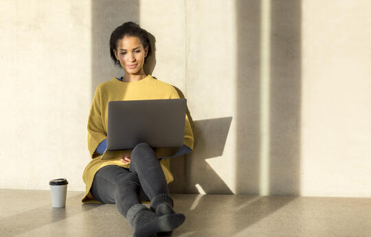 Portrait of smiling young woman sitting on the floor using laptop